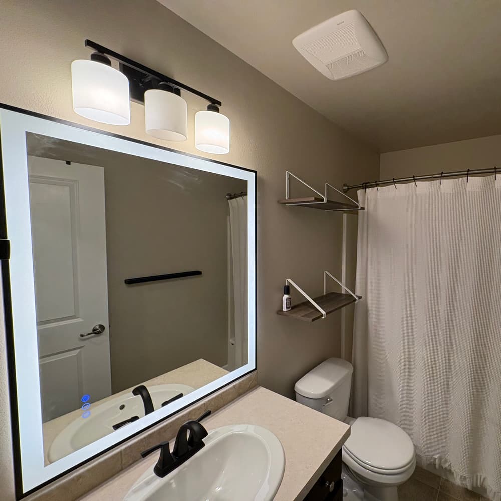 The finished bathroom with a backlit mirror, new vanity light, shelving and freshly painted walls